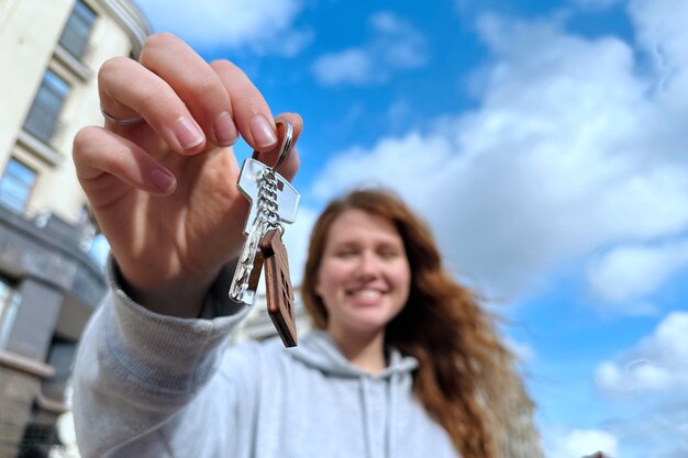 Foto jonge vrouw houdt een sleutel in haar uitgestrekte hand staande op de straat tegen de achtergrond van een
