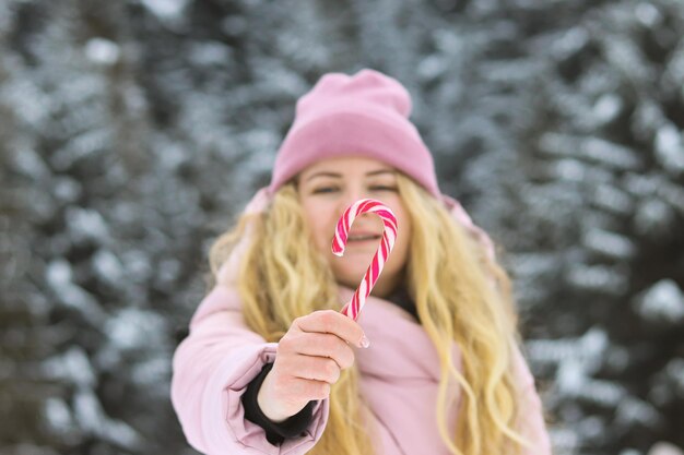 Foto jonge vrouw houdt een zuurstok in haar hand tegen het winterboslandschap focus op de voorgrond