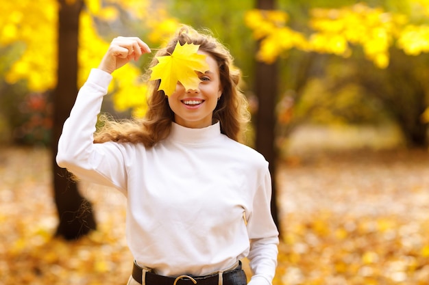 Jonge vrouw houdt geel blad in haar hand met een glimlach in het park bij zonsondergang