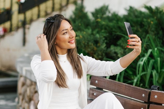 Jonge vrouw houdt haar telefoon tegen haar gezicht en glimlacht Concept van geluk en genot terwijl de vrouw een selfie maakt