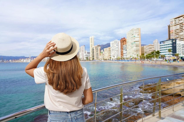 Jonge vrouw houdt hoed op promenade voor de skyline van Benidorm Downtown, Spanje