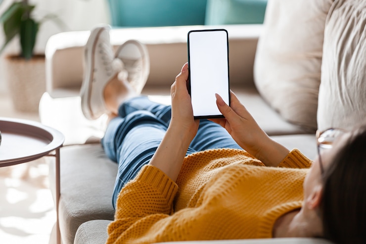 Foto jonge vrouw houdt mobiele telefoon in handen, liggend op de bank