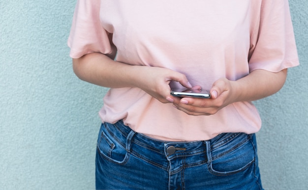 Jonge vrouw houdt smartphone in haar handen op pastel muur