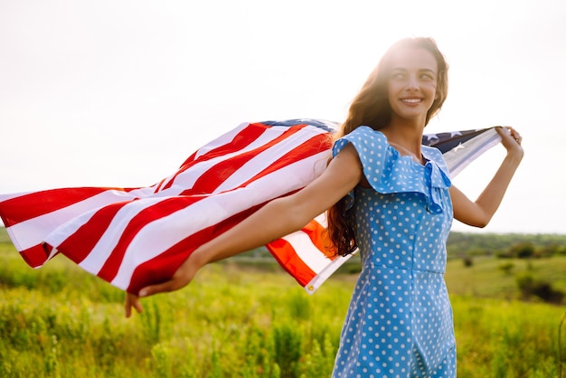 Foto jonge vrouw houdt trots zwaaiende amerikaanse vlag van de vs vast op bloeiende weide 4 juli onafhankelijkheidsdag