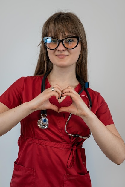 Jonge vrouw huisarts of arts in rood uniform en stethoscoop geïsoleerd op grijs