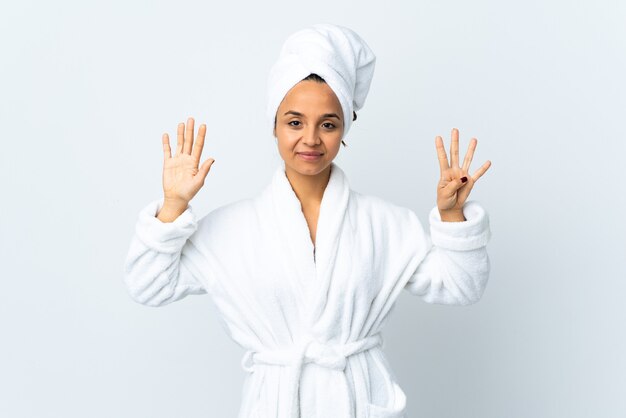Jonge vrouw in badjas over geïsoleerd wit dat negen met vingers telt