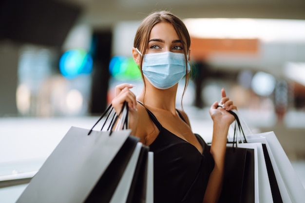 Jonge vrouw in beschermend steriel medisch masker op haar gezicht met boodschappentassen in het winkelcentrum.