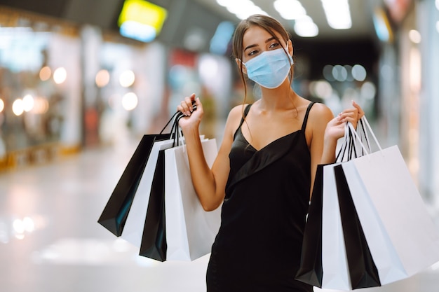 Jonge vrouw in beschermend steriel medisch masker op haar gezicht met boodschappentassen in het winkelcentrum.