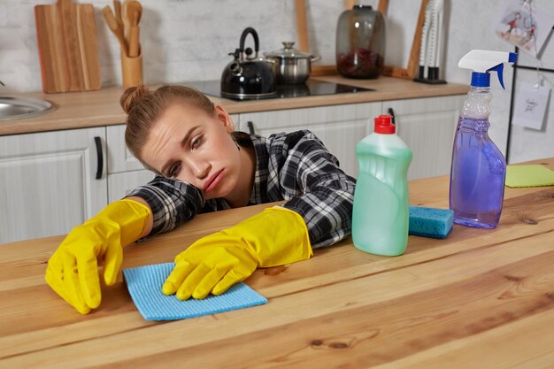 Jonge vrouw in beschermende handschoenen veegt een tafel in de keuken af met een vod