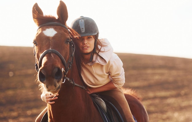 Jonge vrouw in beschermende hoed met haar paard in landbouwveld op zonnige dag