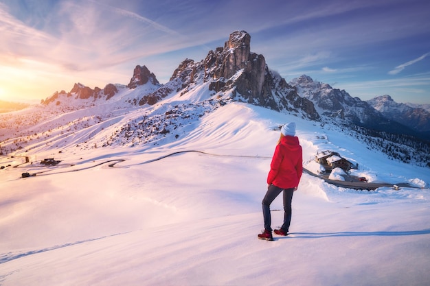 Jonge vrouw in besneeuwde bergen bij zonsondergang in de winter Landschap met mooi meisje op de heuvel besneeuwde rotsen kleurrijke hemel de avond Bergpas Passo Giau Dolomieten Italië Toerisme Reizen