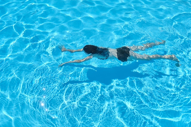 Jonge vrouw in bikini onderwater zwemmen in een buitenzwembad, bovenaanzicht.