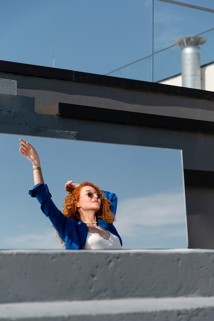 Foto jonge vrouw in blauw pak poseren met spiegel buitenshuis