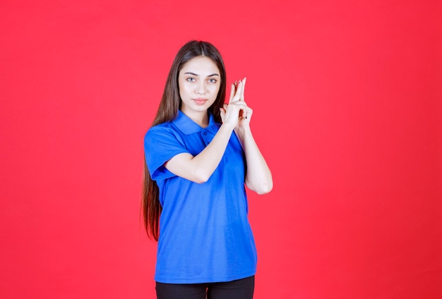 Jonge vrouw in blauw shirt die op de rode muur staat en er verward en attent uitziet