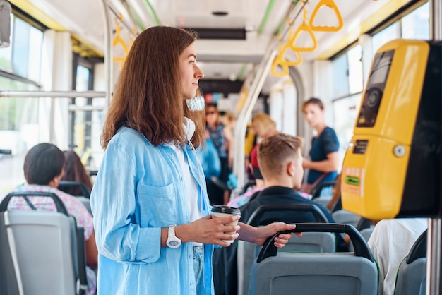 Jonge vrouw in blauw shirt rijdt in de moderne tram of bus met een kopje koffie te gaan.