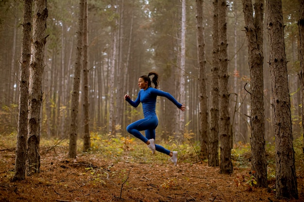 Jonge vrouw in blauw trainingspak die in de herfst hoogspringt op het bospad