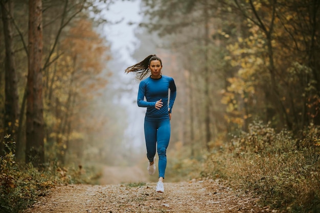 Foto jonge vrouw in blauw trainingspak loopt naar camera op het bospad in de herfst