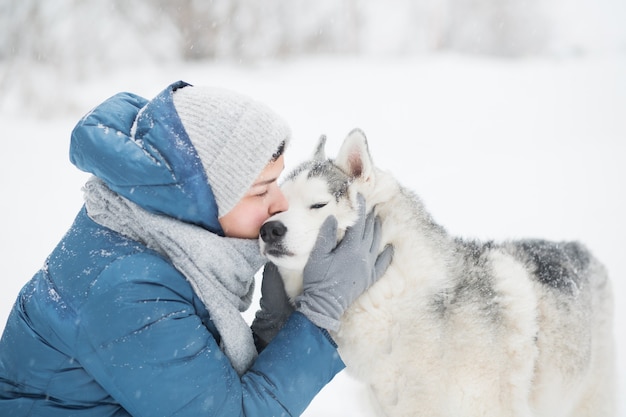 Jonge vrouw in blauwe jas kust besneeuwde Siberische husky in de winter