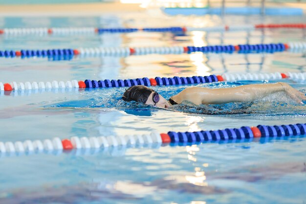 Jonge vrouw in bril en pet zwemmen borstcrawl slag stijl in het blauwe water indoor race zwembad