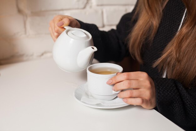 Jonge vrouw in café die hier favoriete drankthee drinkt in witte kop