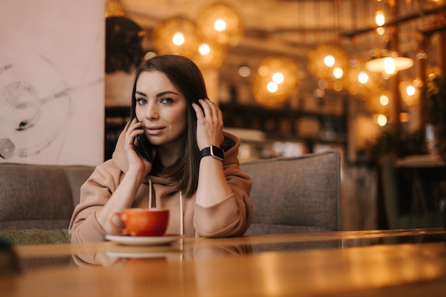 Jonge vrouw in casual kleding zittend aan tafel in café praten op mobiele telefoon