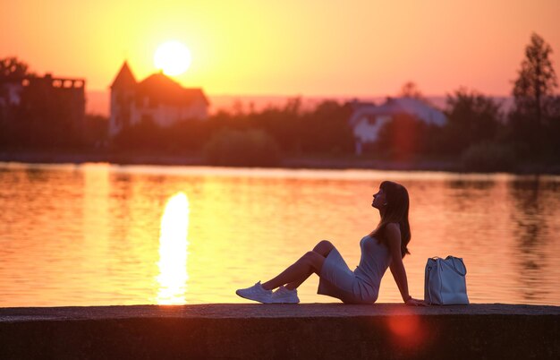 Jonge vrouw in casual outfit ontspannen aan de kant van het meer op warme avond. zomervakanties en reizen concept.