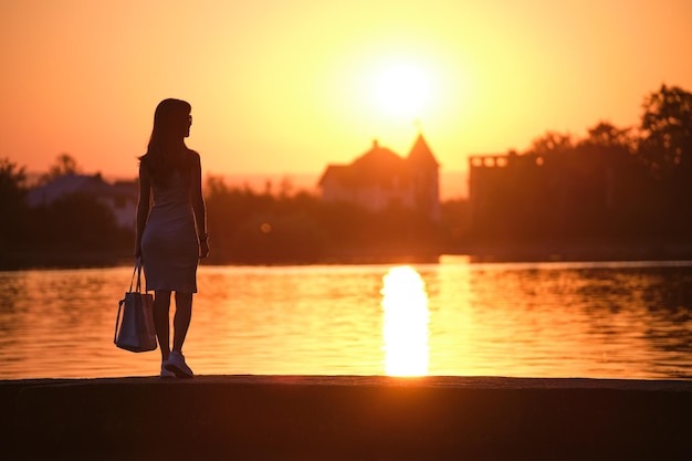 Jonge vrouw in casual outfit ontspannen aan de kant van het meer op warme avond. Zomervakanties en reizen concept.