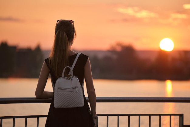 Jonge vrouw in casual outfit ontspannen aan de kant van het meer op warme avond Zomervakanties en reizen concept