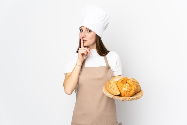 Jonge vrouw in chef-kok uniform op witte muur stilte gebaar doen