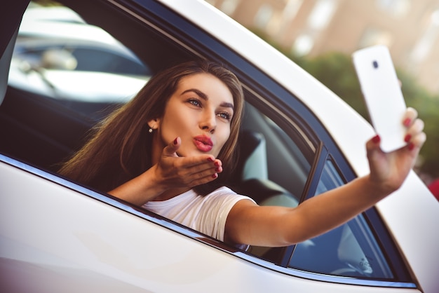 Jonge vrouw in de auto die op vakantie gaat terwijl een passagier selfie maakt.