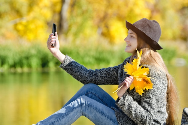 Jonge vrouw in de hoed zittend op het dok en maakt selfie