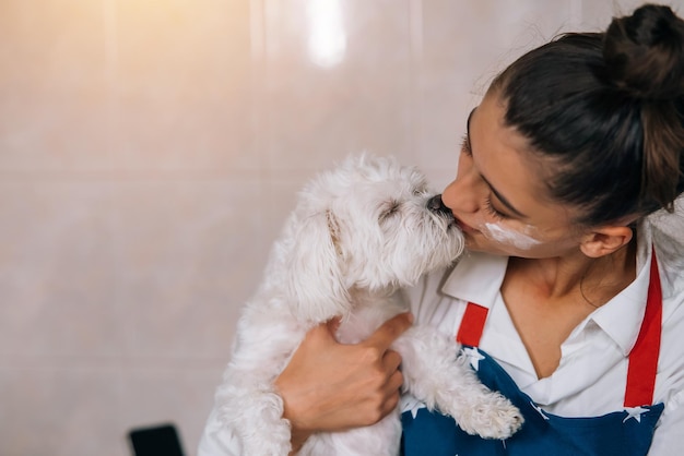 Jonge vrouw in de keuken die een schattige witte Maltese hond kust