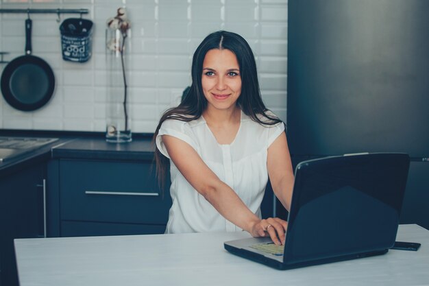 Jonge vrouw in de keuken die met laptop werkt