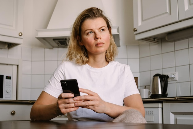 Jonge vrouw in de keuken die met smartphone werkt