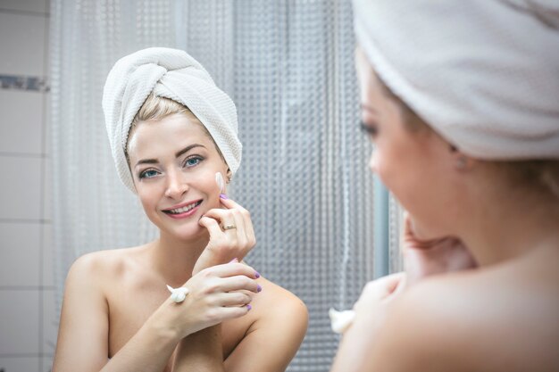 Jonge vrouw in een badkamer heeft cosmetische ingrepen om schoonheid en gezondheid in een handdoek te verbeteren