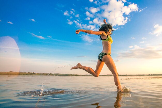 Jonge vrouw in een badpak met krullend haar dat op het water loopt tegen de achtergrond van een blauwe lucht met wolken