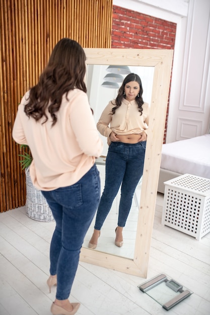 Jonge vrouw in een beige blouse die naar zichzelf kijkt