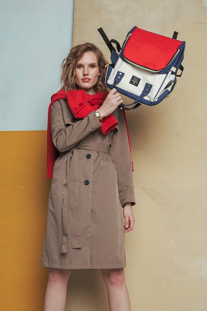 Foto jonge vrouw in een beige trenchcoat met rood-witte rugzak.