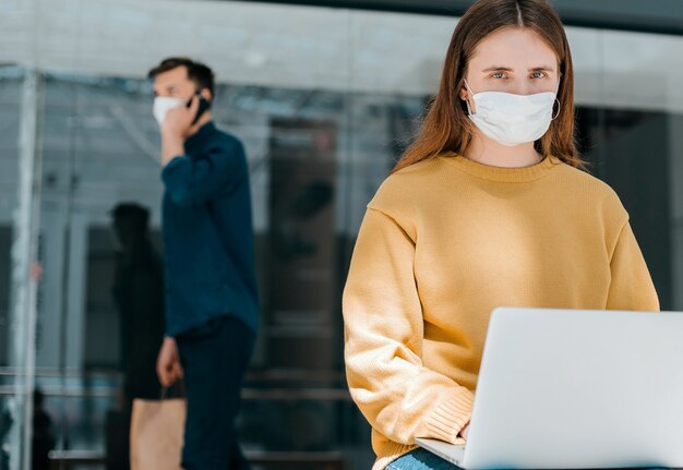 Jonge vrouw in een beschermend masker gebruikt haar laptop op straat