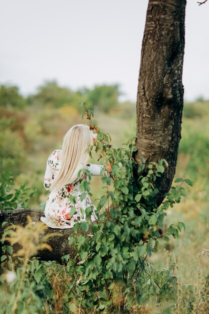 Jonge vrouw in een bloemenjurk zittend op een boom