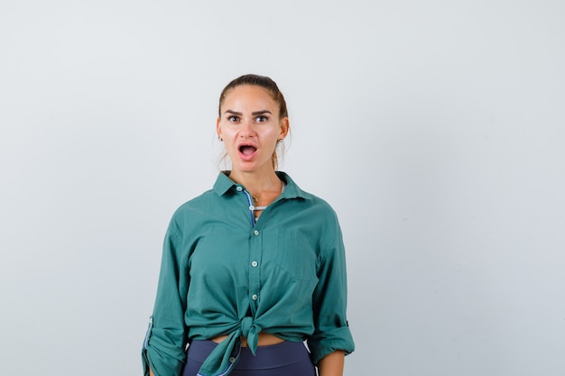 Jonge vrouw in een groen shirt die naar de camera kijkt en zich afvraagt, vooraanzicht.