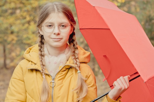 Jonge vrouw in een herfstpark met een rode paraplu, draaiend en een paraplu vasthoudend, herfstwandeling in een geel oktoberpark
