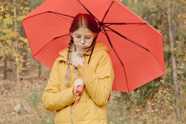 Jonge vrouw in een herfstpark met een rode paraplu, draaiend en een paraplu vasthoudend, herfstwandeling in een geel oktoberpark