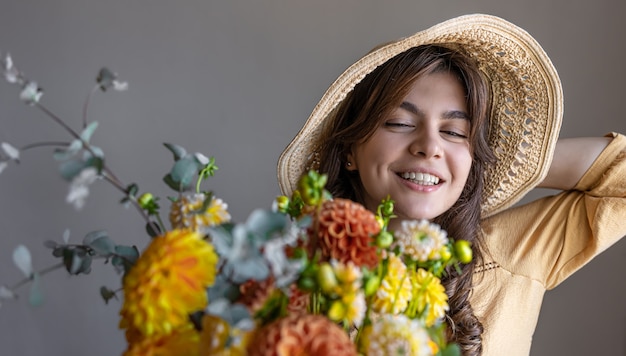 Jonge vrouw in een hoed met een boeket chrysanten op een grijze achtergrond