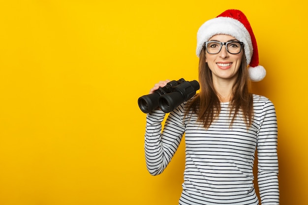 Jonge vrouw in een kerstman hoed houdt een verrekijker