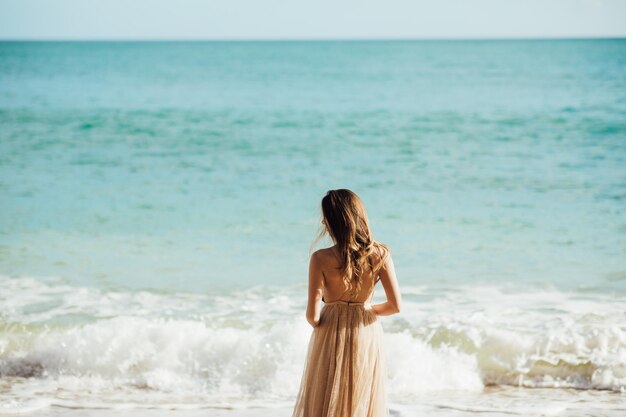 jonge vrouw in een lange jurk wandelen op het strand in de buurt van de oceaan.