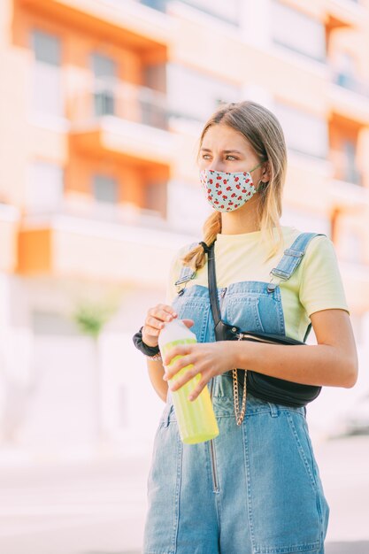 Jonge vrouw in een masker drinkwater en wandelen door de stad