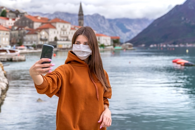 Jonge vrouw in een medisch masker neemt een selfie op straat van een Europese stad.