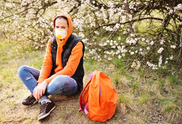 Jonge vrouw in een oranje sweatshirt met capuchon en een gasmasker of masker