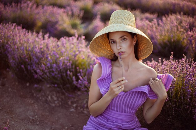 Jonge vrouw in een paarse korte jurk en een strohoed staat in een veld met lavendel op de Krim bij zonsondergang